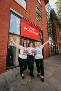 Amelia Sutcliffe, Sammi Allen and Katie Bullimore stand in front of the Smith Partnership Solicitors head office in Friar Gate Derby wearing T-shirts with sponsors names on