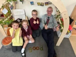 Image shows Year 1 pupils Noah (wearing yellow shirt), Harriet and Oliver with head teacher David Blackwell