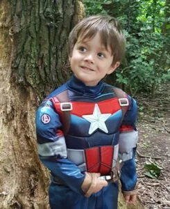 the photo is of 5 year old boy Sam who is dressed in a captain America costume stood in front of a tree