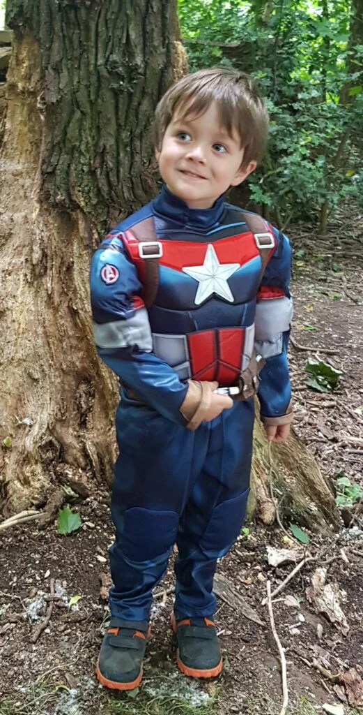 the photo is of 5 year old boy Sam who is dressed in a captain America costume stood in front of a tree