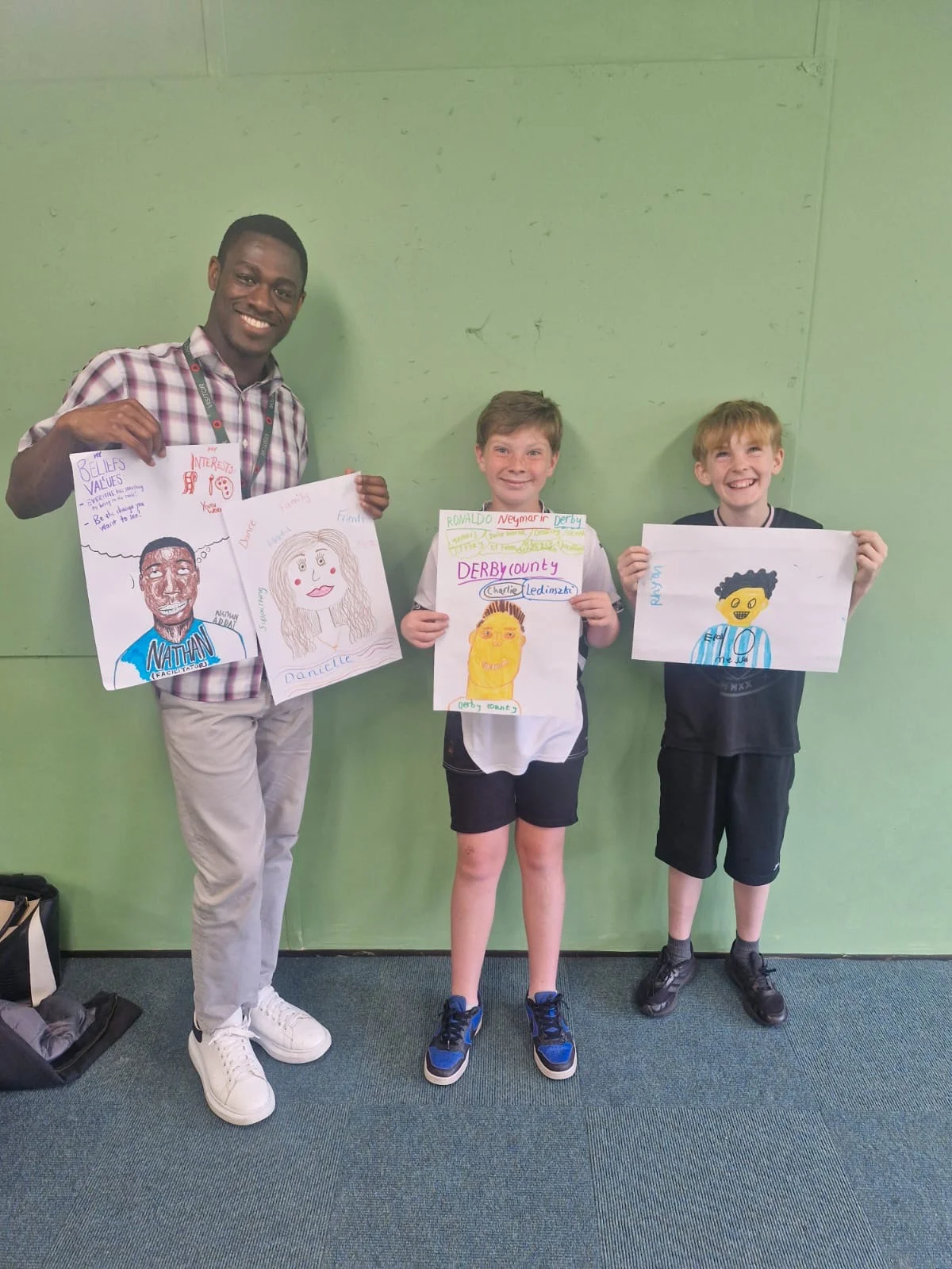 Nathan, facilitator at Freedom Foundation standing holding artwork with two pupils at the Alternative Provision set up at Portway Junior School
