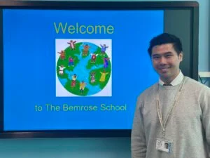Leo Chan who is a teacher at Bemrose School standing infront of the interactive whiteboard that is depicting a logo
